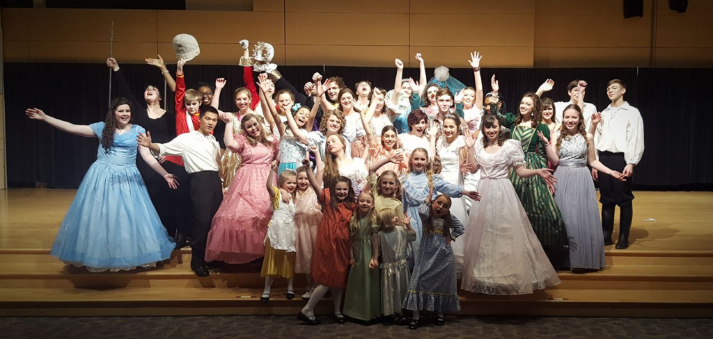 A joyful group of children and adults in colorful costumes on stage.